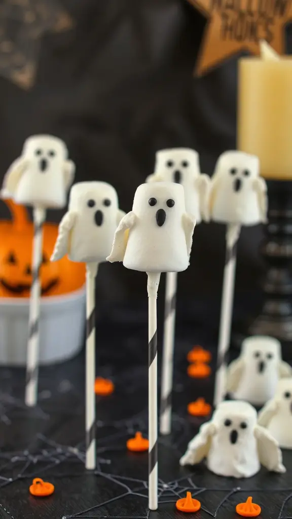 A display of ghost-shaped marshmallow pops on sticks, decorated with black icing eyes and mouths, set against a Halloween-themed background.