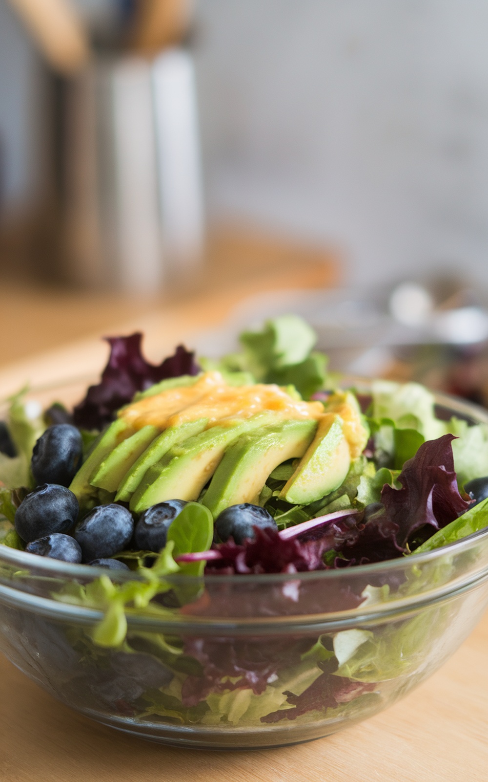 A fresh Blueberry Avocado Salad with greens, sliced avocado, and blueberries in a glass bowl.